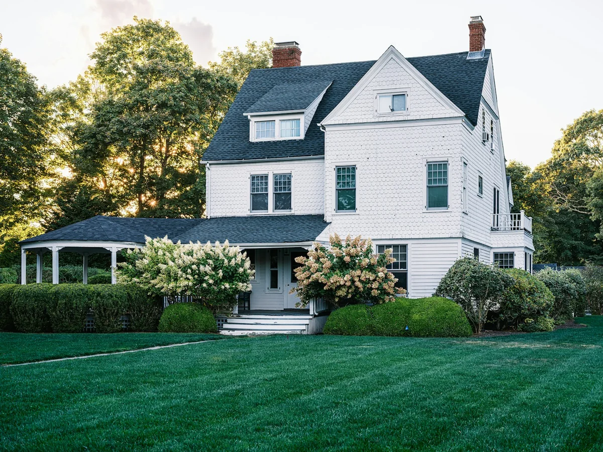 White residential house with a welcoming porch, landscaped garden and green lawn